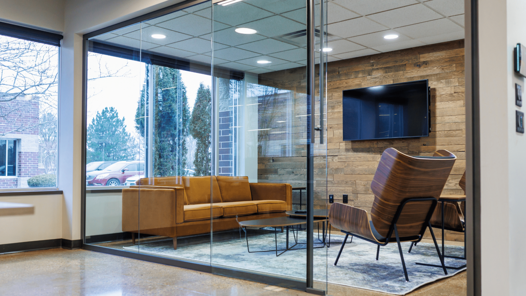 Glass Tknion architectural walls compliment a modern office space that contains leather couch and chairs.