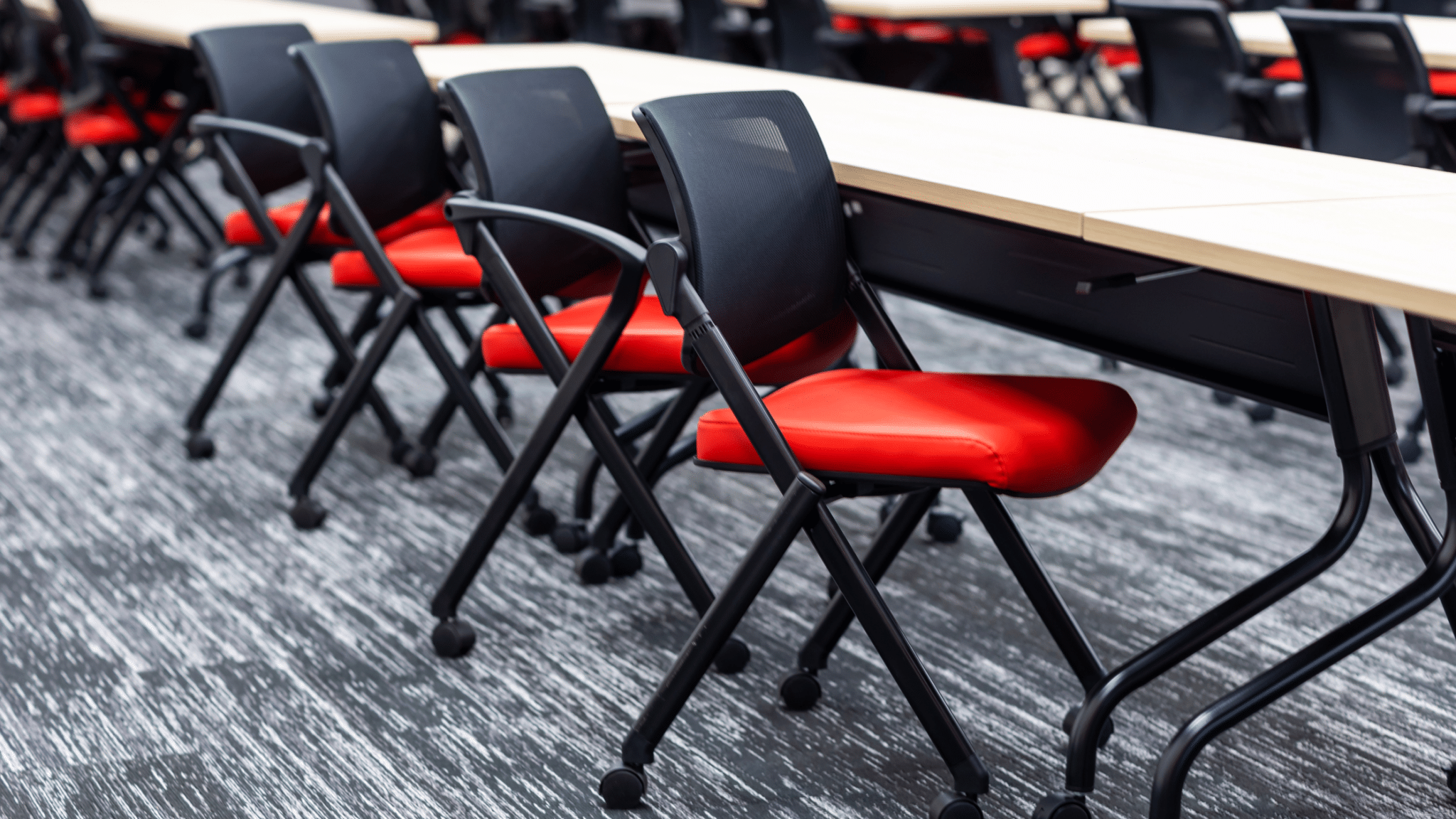 A row of black office chairs with bright red seats are lined up at a table in a modern, contemporary office space.